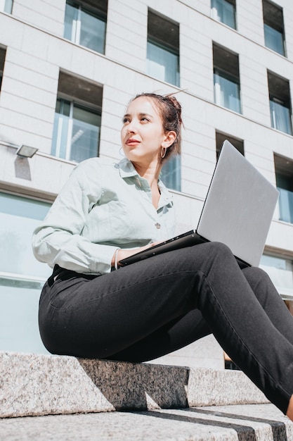 Młody Afroamerykanin Businesswoman siedzi na schodach na zewnątrz pracy na laptopie w jasny dzień. Udane freelancer pisania na klawiaturze przy użyciu laptopa. Portret kobiety copywriter