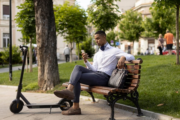 Młody Afroamerykanin korzystający z telefonu komórkowego siedząc na ławce skutera elektrycznego