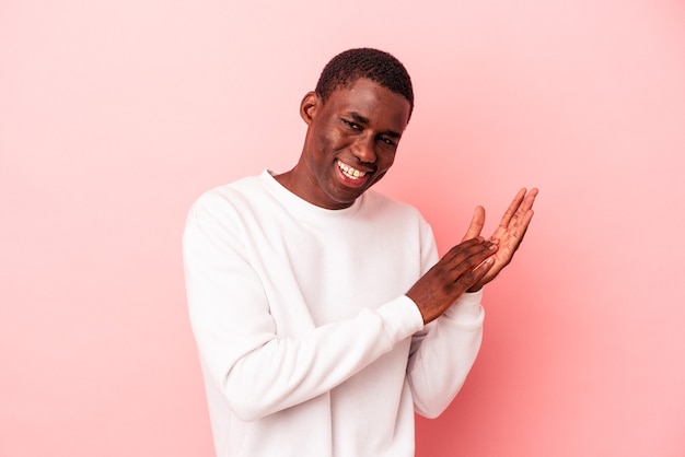 Młody Afroamerykanin na białym tle na różowym tle czuje się energiczny i wygodny, zacierając ręce pewnie.