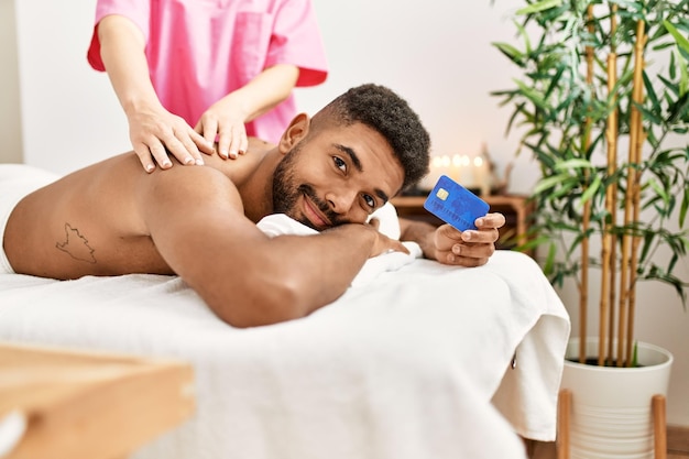 Młody Afroamerykanin odzyskujący masaż pleców i posiadający kartę kredytową w centrum urody.