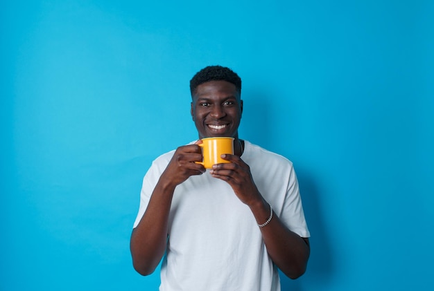 Młody Afroamerykanin Pije Kawę Z żółtej Filiżanki Na Niebieskim Tle