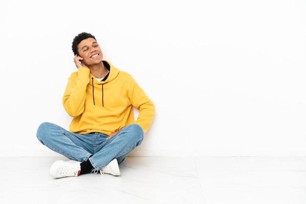 Młody Afroamerykanin siedzący na podłodze na białym tle myślący o pomyśle