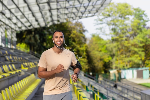 Młody afroamerykanin sportowiec lekkoatleta biegający w słuchawkach na stadionie