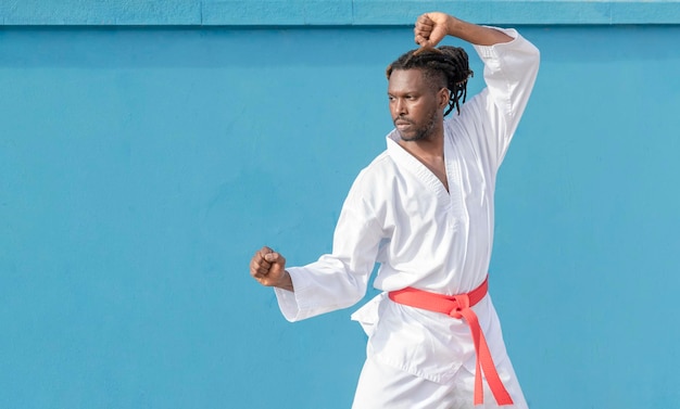 Młody Afroamerykanin trenuje taekwondo na świeżym powietrzu na niebieskim tle
