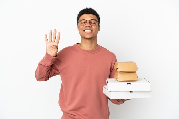 Młody Afroamerykanin trzymający burgera i pizze na białym tle szczęśliwy i liczący cztery palcami
