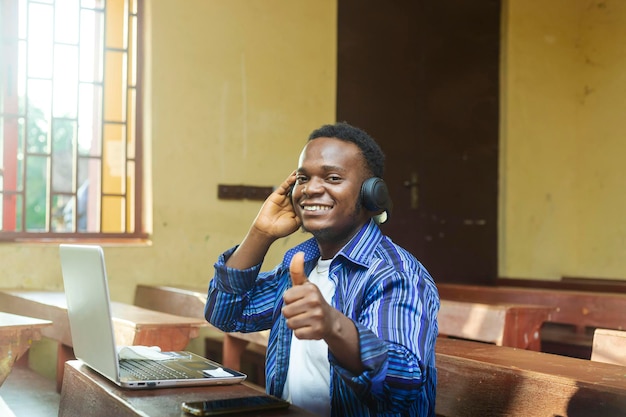Młody afrykański biznesmen uśmiechający się, podnoszący rękę, by unieść kciuki ku zadowoleniu klienta
