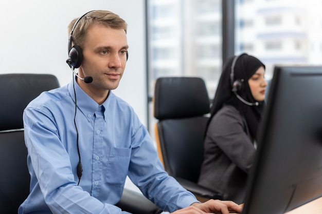 Młody agent obsługi klienta ze słuchawkami pracujący na komputerze w call center, rozmawiający z klientem za pomoc w rozwiązaniu problemu z jej umysłem obsługi