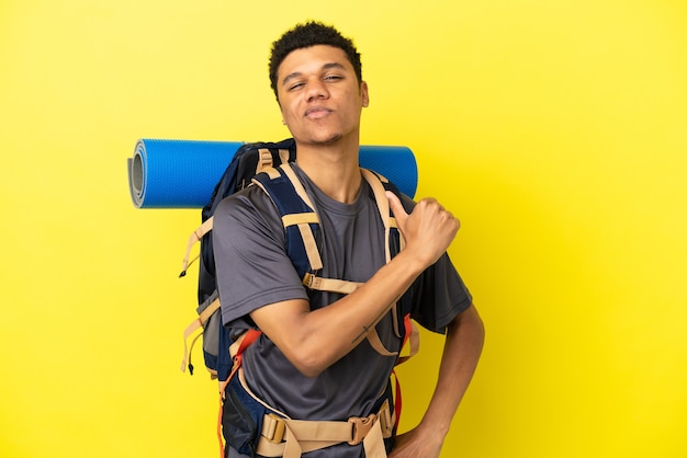 Młody alpinista Afroamerykanin z dużym plecakiem na żółtym tle dumny i zadowolony z siebie