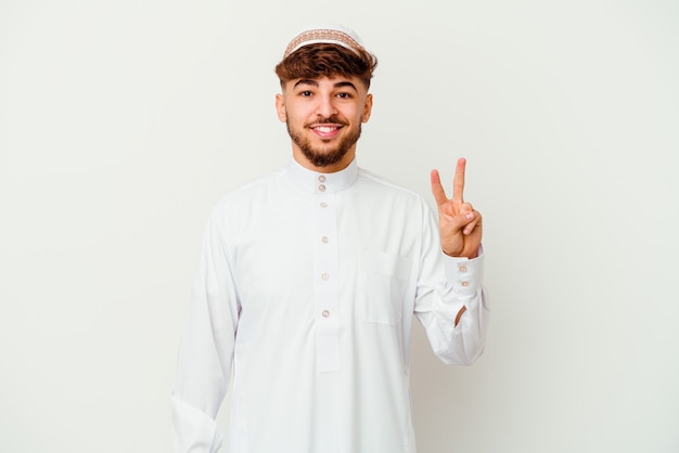 Młody Arabski mężczyzna ubrany w typowy strój arabski na białym tle na białej ścianie pokazuje numer dwa palcami.