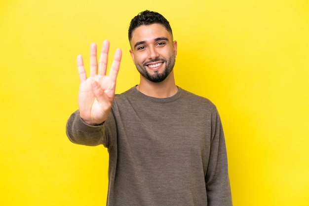 Młody arabski przystojny mężczyzna odizolowany na żółtym tle szczęśliwy i liczący cztery palcami