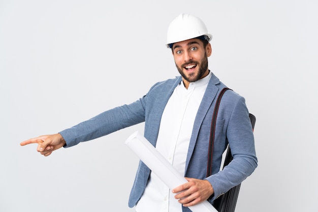 Młody architekt mężczyzna z hełmem i trzymając plany na białym palcem wskazującym na bok i prezentacji produktu na białym tle