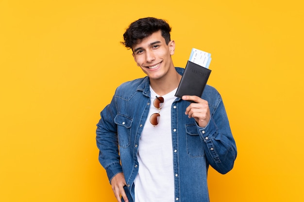 Młody Argentyński mężczyzna nad odosobnionym żółtym tłem szczęśliwym w wakacje z paszportem i samolotowymi biletami