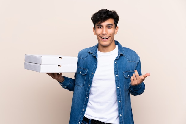 Młody Argentyński mężczyzna trzyma pizze nad odosobnioną ścianą z szokującym wyrazem twarzy
