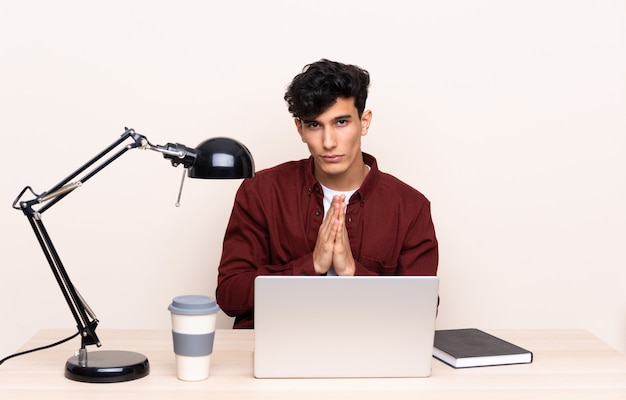 Młody Argentyński mężczyzna w stole z laptopem w jego miejscu pracy błagać
