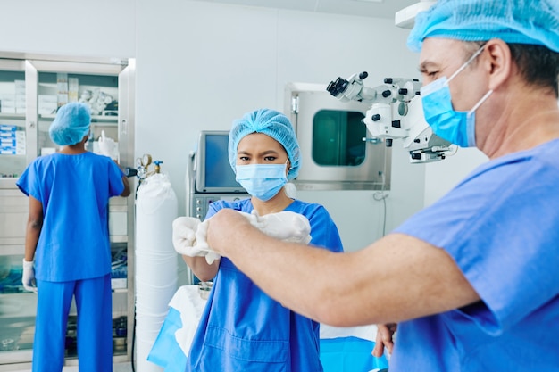 Młody asystent pomagający chirurgowi założyć sterylne rękawiczki chirurgiczne na sali operacyjnej