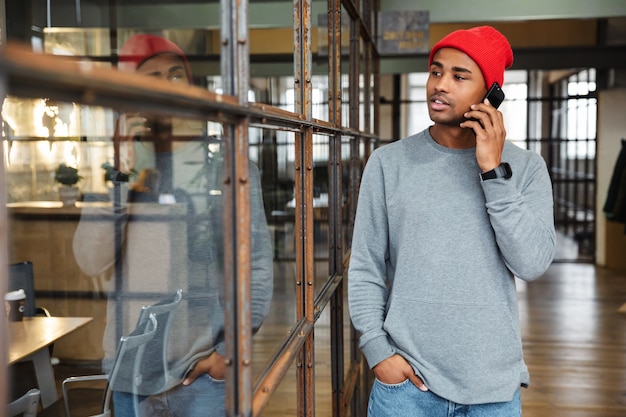 młody atrakcyjny afroamerykanin w kapeluszu rozmawiający przez telefon podczas pracy w biurze