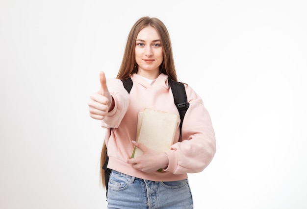 Młody atrakcyjny caucasian kobieta student z plecakiem i książkami pokazuje kciuk up odizolowywający na białym tle