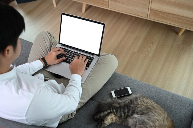 Młody atrakcyjny mężczyzna siedzi na kanapie w domu podczas pracy na laptopie w Internecie