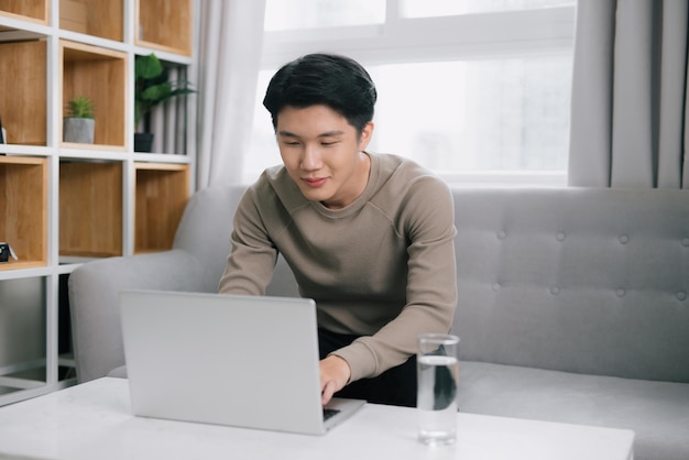 Młody atrakcyjny mężczyzna siedzi na kanapie w domu pracuje na laptopie online freelancer wolny czas wolny