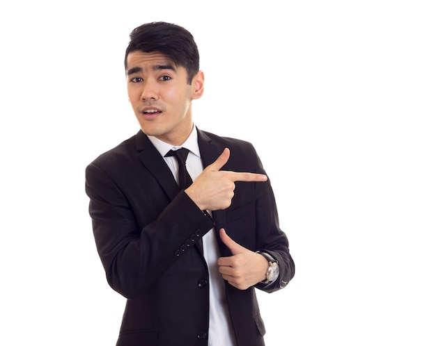 Młody atrakcyjny mężczyzna w czarnym smokingu z czarnym krawatem i drogim zegarkiem wskazującym na coś