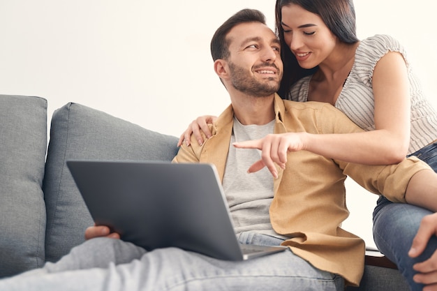 Młody, atrakcyjny, uroczy mężczyzna i kobieta spędzają razem wolny czas i siedząc na kanapie podczas korzystania z laptopa