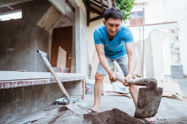 Zdjęcie młody azjat pracuje nad mieszanką cementową, używając szotki do budowy betonowej ściany domu