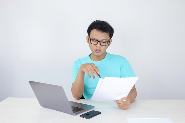 Młody Azjata jest poważny i skupia się podczas pracy na laptopie i dokumentu na stole Indonezyjski mężczyzna w niebieskiej koszuli