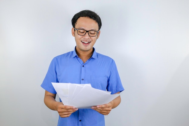 Młody Azjata Jest Uśmiechnięty I Szczęśliwy, Patrząc Na Papierowy Dokument Indonezyjski Mężczyzna W Niebieskiej Koszuli