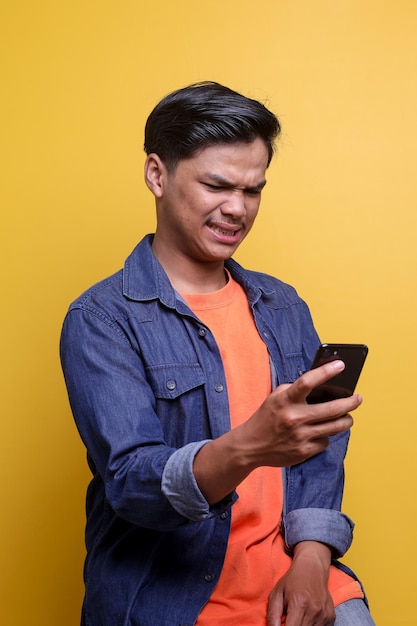 Młody Azjata patrzący na telefon komórkowy z obrzydliwym wyrazem twarzy Wyraz twarzy ludzkich emocji