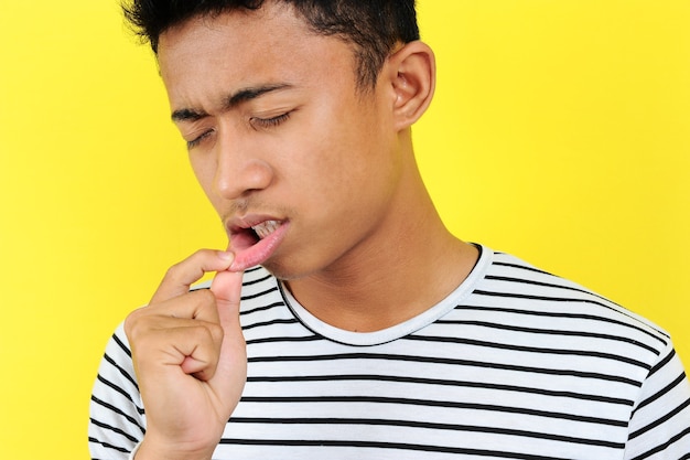 Młody Azjata pokazujący wrzód lub pęcherz w ustach przed kamerą, odizolowany na żółtym tle