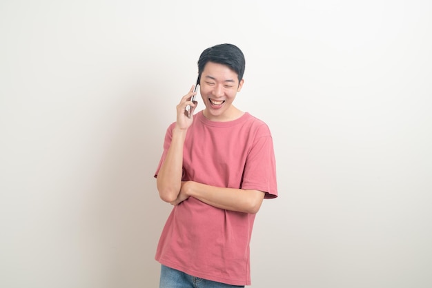 młody Azjata używający lub mówiący smartfonem i telefonem komórkowym z szczęśliwą twarzą na białym tle