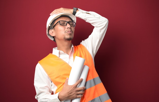 Młody azjatycki architekt trzymający papierowy plan projektu zszokowany ręką na głowie i sfrustrowany
