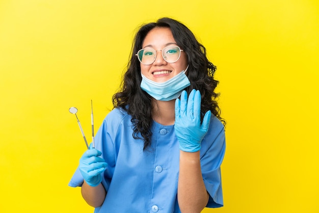Młody Azjatycki Dentysta Posiadający Narzędzia Na Na Białym Tle Zapraszając Z Ręką. Szczęśliwy, że Przyszedłeś