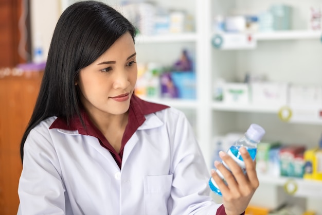 Młody azjatycki farmaceuta patrząc butelka niebieski żel pod ręką w aptece