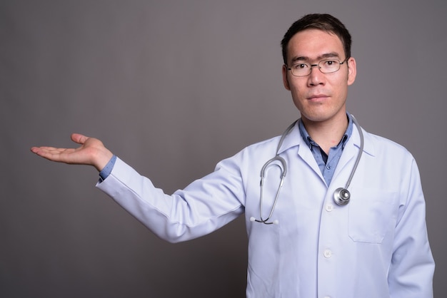 Młody azjatycki lekarz człowiek przed szarej ścianie