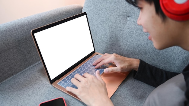 Młody azjatycki mężczyzna noszący słuchawki używający laptopa na kanapie