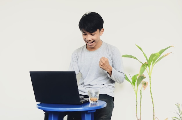 Młody azjatycki mężczyzna siedzący przy laptopie z zadowolonym wyrazem twarzy
