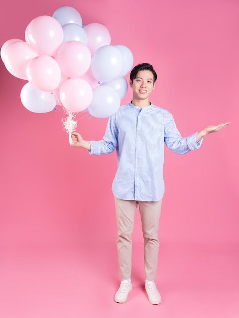 Młody azjatycki mężczyzna trzyma balon na różowym tle
