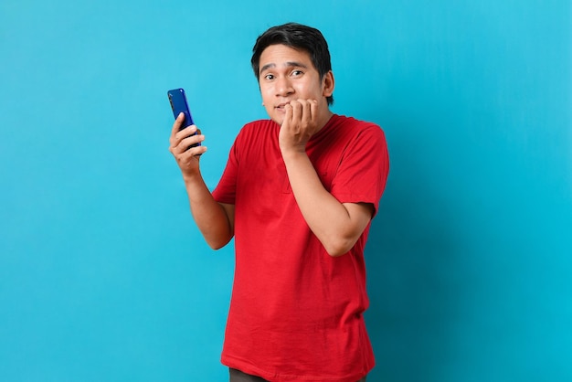 Młody Azjatycki mężczyzna trzyma telefon komórkowy z szokującym wyrazem twarzy