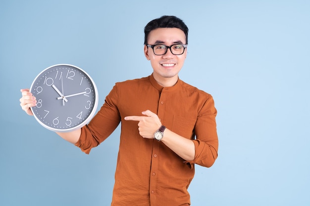 Młody azjatycki mężczyzna trzyma zegar na niebieskim tle