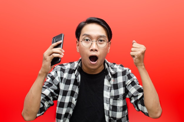 młody azjatycki mężczyzna trzymający telefon w różnych wypowiedziach smutny, szczęśliwy, zszokowany, zły na białym tle nad czerwonym.