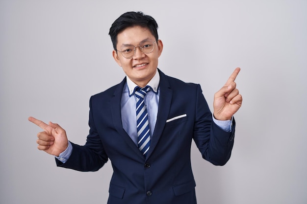 Młody azjatycki mężczyzna w garniturze i krawacie uśmiecha się pewnie, wskazując palcami na różne kierunki. skopiuj miejsce na reklamę