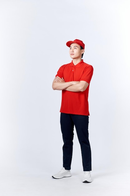 Młody azjatycki mężczyzna w jednolitej czerwieni i czapce stojącej z rękami skrzyżowanymi z pewnym siebie odizolowanym na białym tle