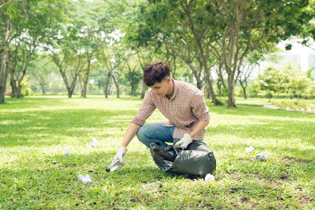 Młody azjatycki mężczyzna w żółtych gumowych rękawiczkach wkłada odpady domowe do małej torby na śmieci