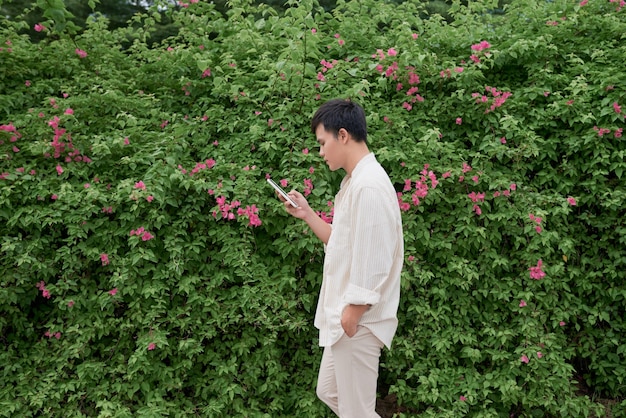 Młody azjatycki mężczyzna w zwykłych ubraniach w letni dzień i za pomocą smartfona do wysyłania sms