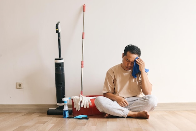 Młody azjatycki mężczyzna zmęczony opierający się o ścianę z produktami czyszczącymi w domu