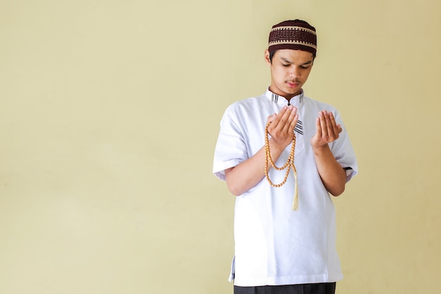 Młody azjatycki muzułmanin modlący się trzymając koraliki różańca z miejsca na kopię