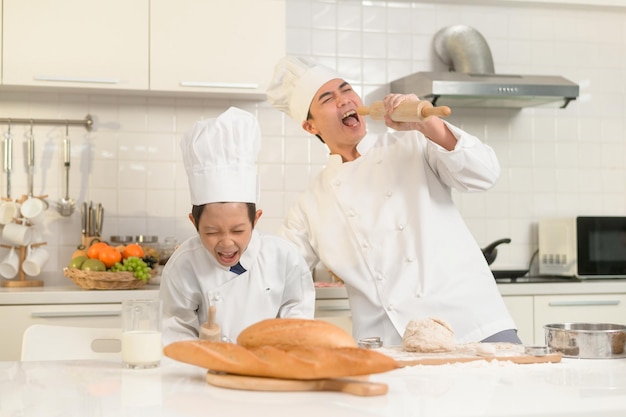 Młody azjatycki ojciec i jego syn w mundurze szefa kuchni pieczą razem w kuchni w domu