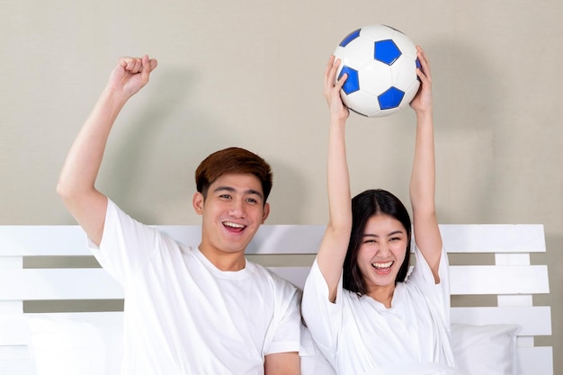 Młody azjatycki przystojny mąż i piękna żona czują się świetnie, gdy piłka nożna, którą kibicują, jest zwycięzcą w sypialni