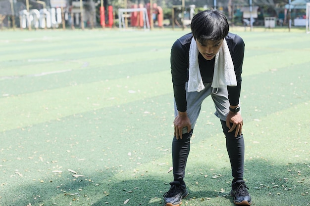 Młody azjatycki sportowiec w odzieży sportowej, trzymający się za kolano, wyczerpany po bieganiu i joggingu